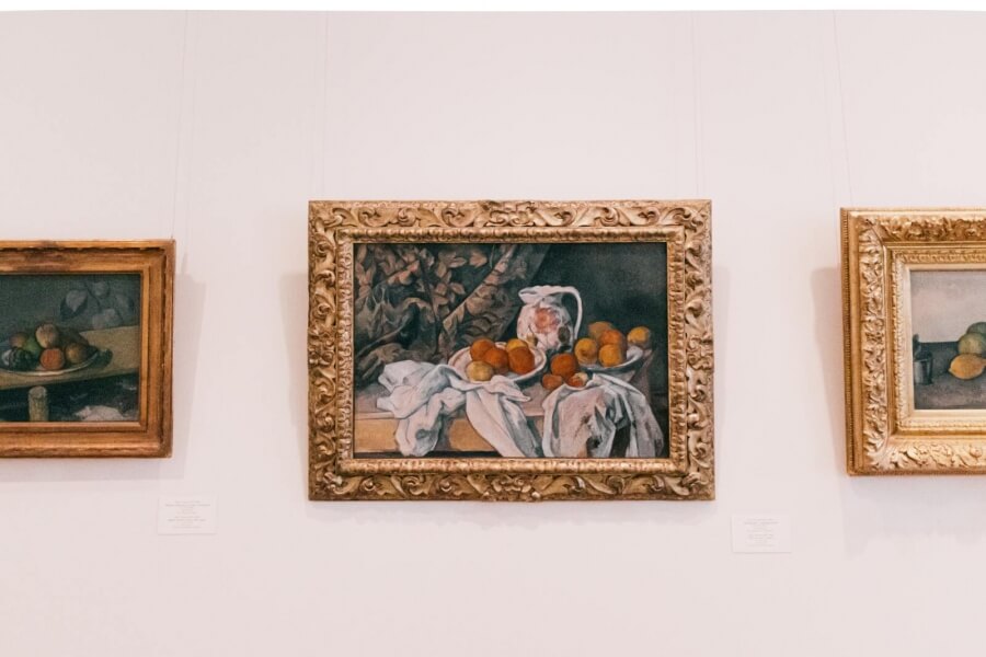 Drei Gemälde im klassischen Stil hängen in einem Museum an einer weißen Wand