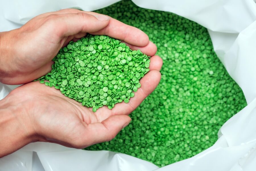 Hände halten grünes Kunststoff-Granulat