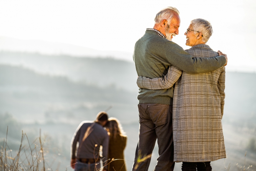 Älteres Ehepaar umarmt sich und stehen dabei auf einem Hügel.