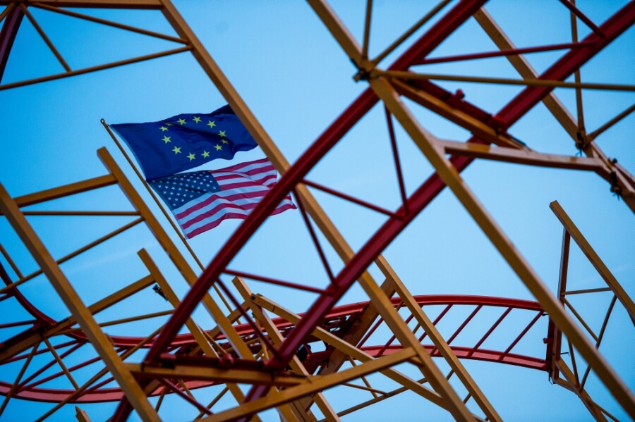 Eine EU-Fahne und eine US-Fahne wehen auf einer noch nicht fertig aufgebauten Achterbahn.