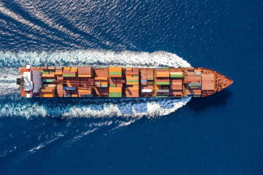 Top down Ansicht auf ein beladenes Containerschiff in voller Fahrt über blauem Meer.