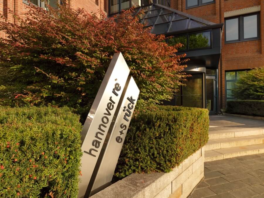 Auf zwei Metallstäben steht der Name Hannover Rück vor dem Bürogebäude des gleichnamigen Unternehmens