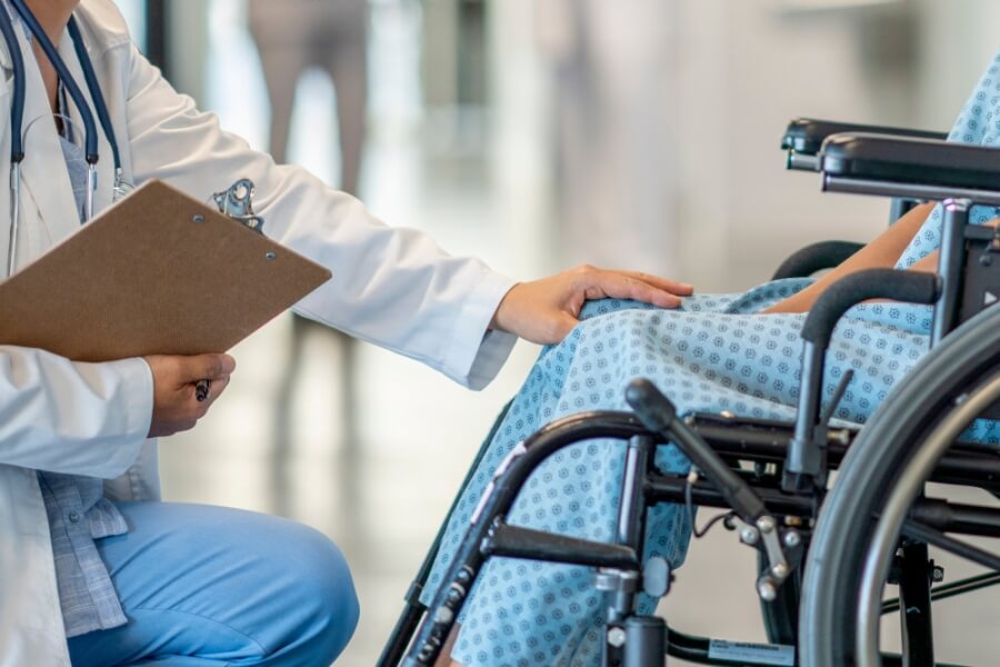 Arzt legt die Hand auf das Knie einer Person im Rollstuhl