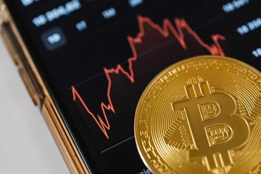 Ein Bitcoin, im Hintergrund eine geöffnete Trading-App