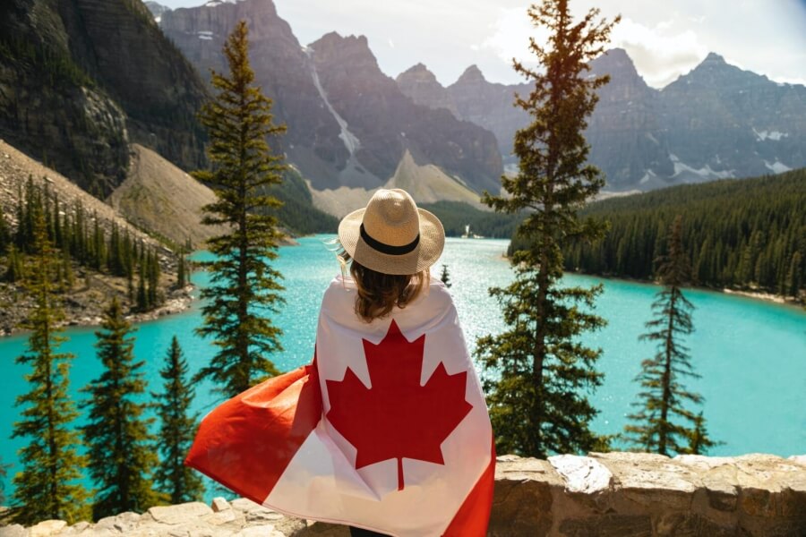 Eine Frau hat sich eine Kanadaflagge um die Taille gewickelt und blickt auf einen Bergsee