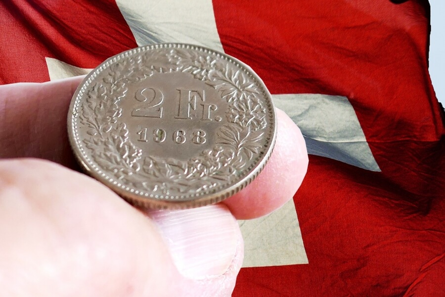 Eine Münze, 2 Schweizer Franken, im Hintergrund die Flagge der Schweiz