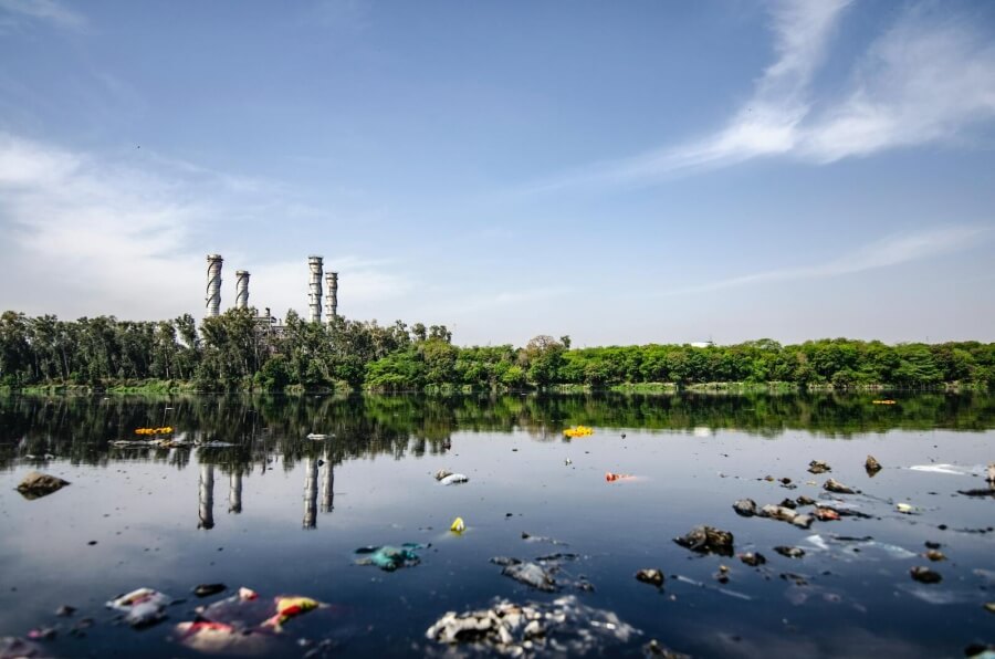 Müll schwimmt auf einem See, im Hintergrund eine Fabrik