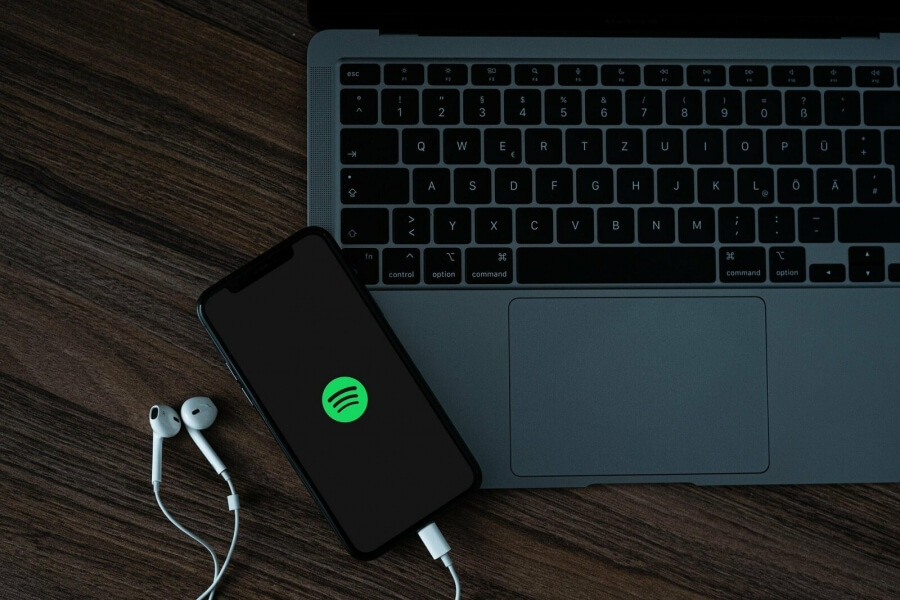 Ein Handy mit geöffneter Spotifyapp liegt auf einem Laptop
