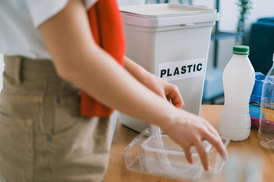 Junge Frau wirft Plastik-Verpackungen in Abfalleimer