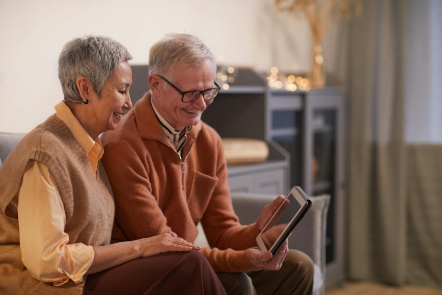 Ein älteres Ehepaar sitzt auf einer Couch und betrachtet ein Tablet