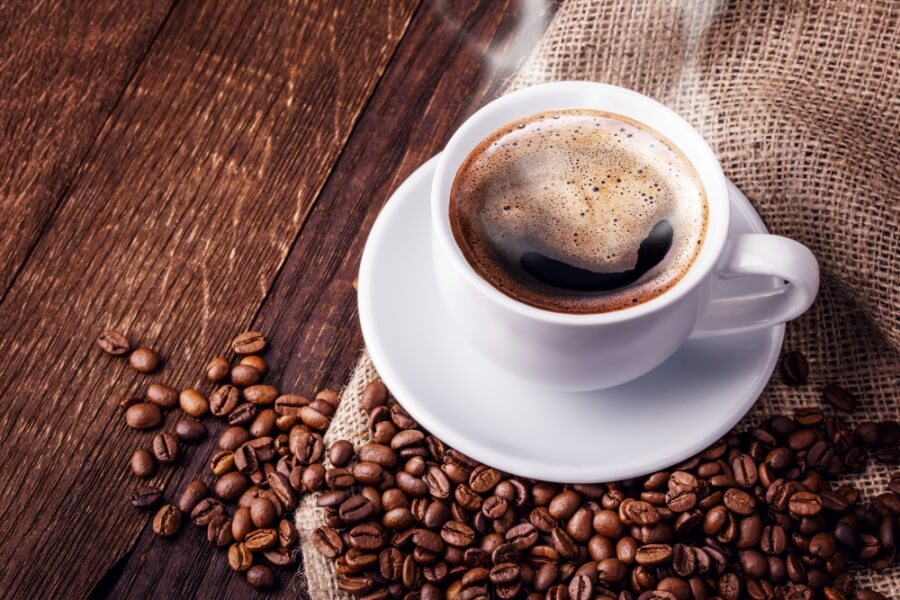 Tasse Kaffee mit umherliegenden Kaffeebohnen