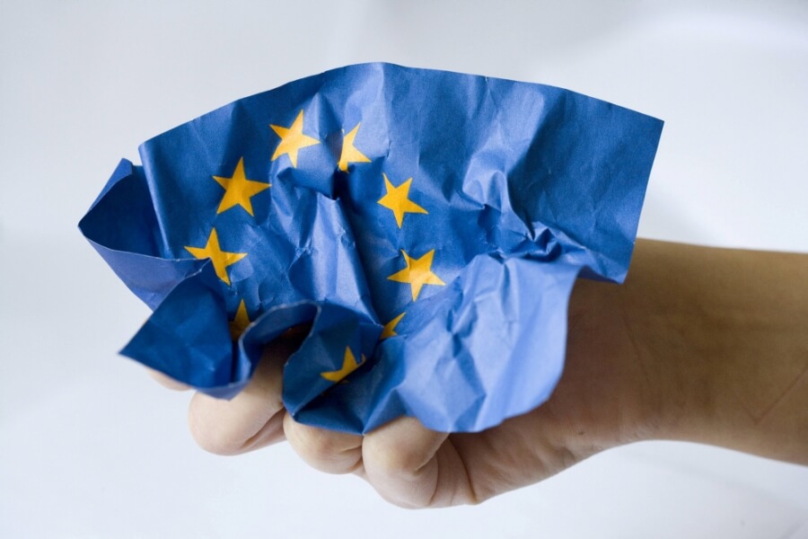 Eine Hand zerknüllt ein blaues Papier mit den gelben Sternen der Europäischen Union