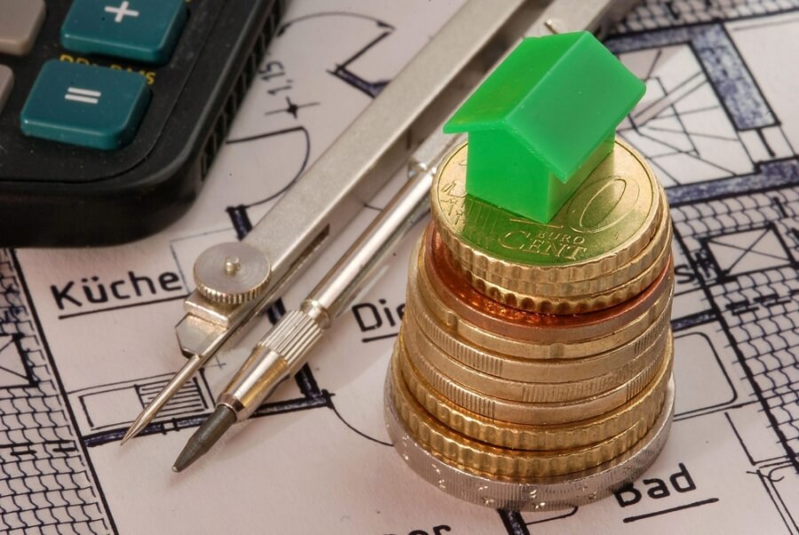 Ein grünes Haus aus dem Monopoly-Spiel steht auf einem Münzstapel
