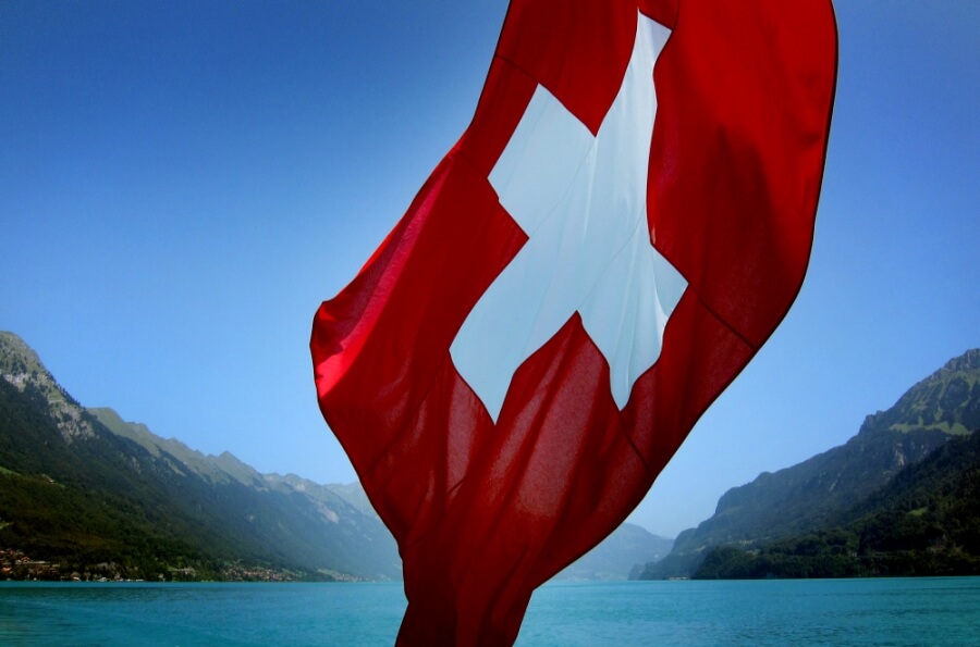 Die Schweizer Flagge weht, im Hintergrund ein Gebirgssee