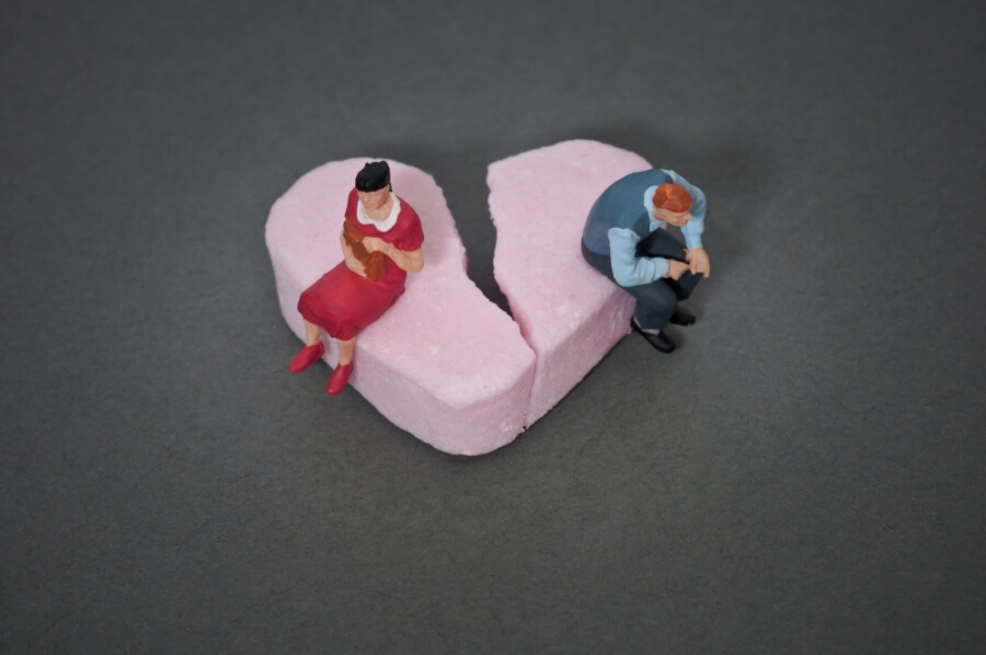 Zwei Personen sitzen auf einem gebrochenen Herz, Symbol für Scheidung / Trennung