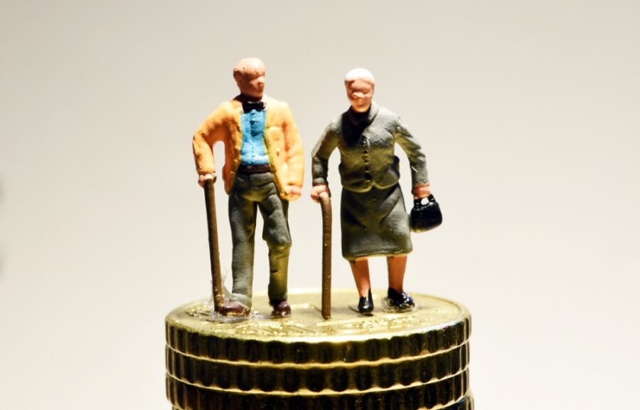 Modellfiguren eines Rentnerpaares stehen auf einem Stapel Münzen.