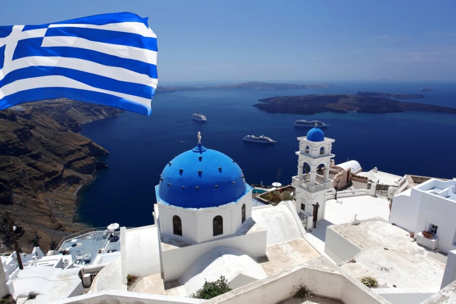 Weiße Häuser mit blauen Dächern und griechischer Flagge an einem griechischen Urlaubsort