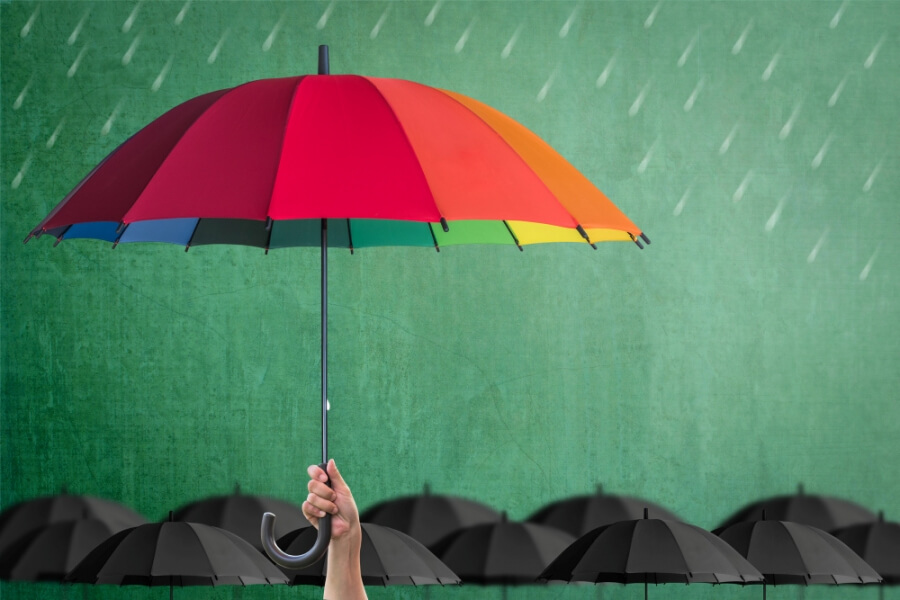 Ein bunter Regenschirm schützt vor Regen, darunter viele schwarze Schirme