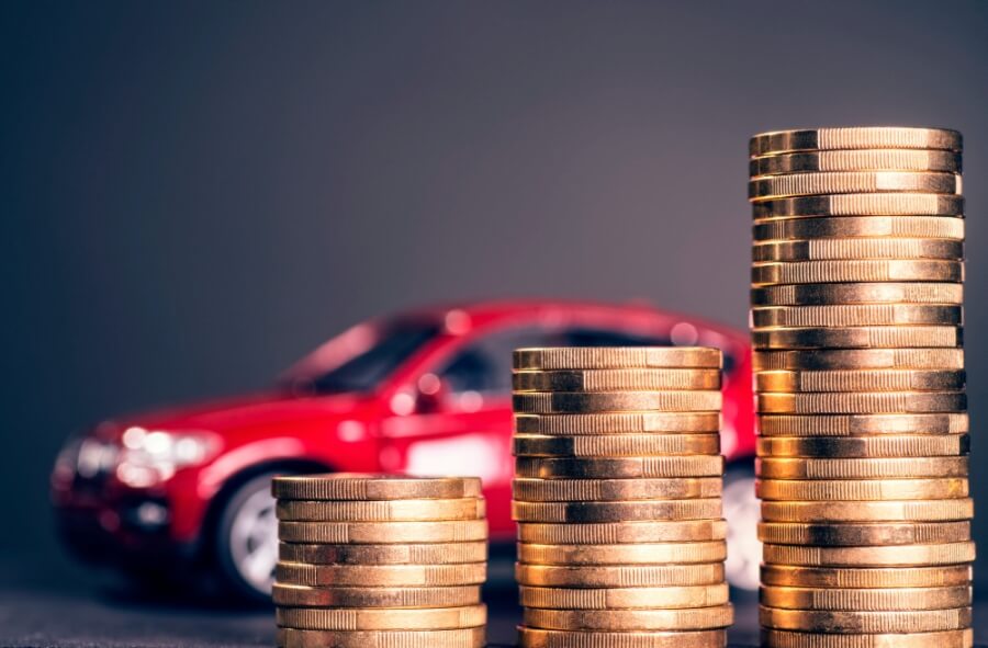 Ansteigende Stapel mit Münzen und einem roten Auto im Hintergrund