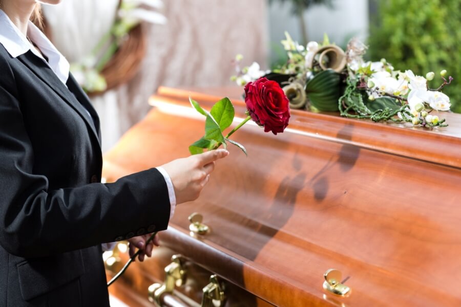 Beerdigung, Person steht mit einer Rose in der Hand an einem Sarg