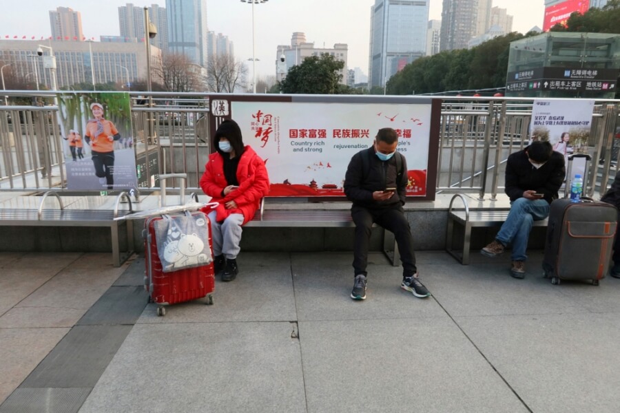 Menschen in Wuhan sitzen mit Masken und Abstand während der Corona-Pandemie auf einer Bank.