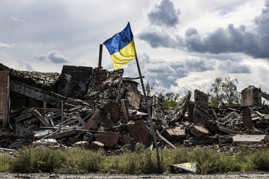 Ukrainische Fahne weht vor den Ruinen zerstörter Häuser