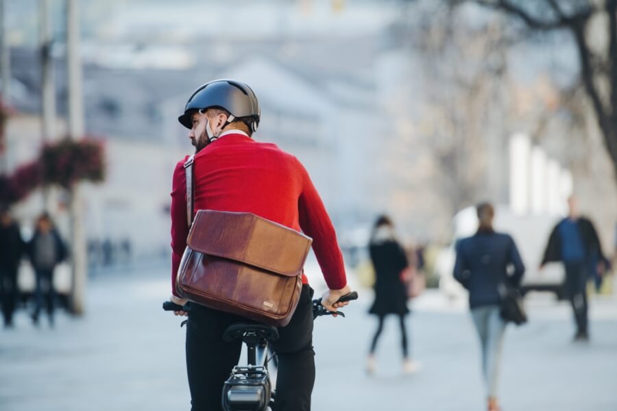 Mann mit rotem Pullover und einer Business-Umhängetasche fährt Fahrrad
