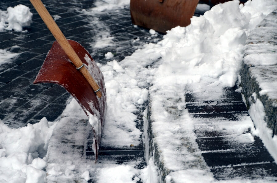 Eine Person befreit mit einer Schneeschippe eine Treppe von Schnee