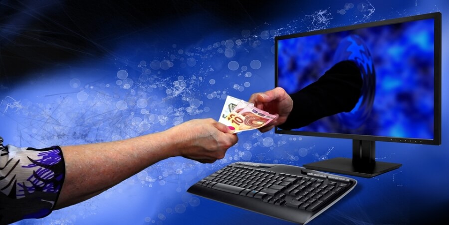 Eine Hand reicht Geldscheine einer anderen Hand, die aus einem PC-Bildschirm ragt.