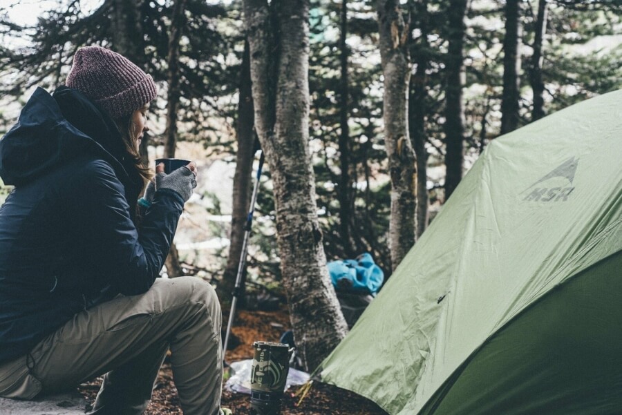 Eine Camperin trinkt Tee vor einem Zelt
